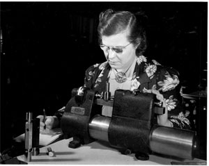 Woman at table using large caliper to check cylindrical spiral threaded gage